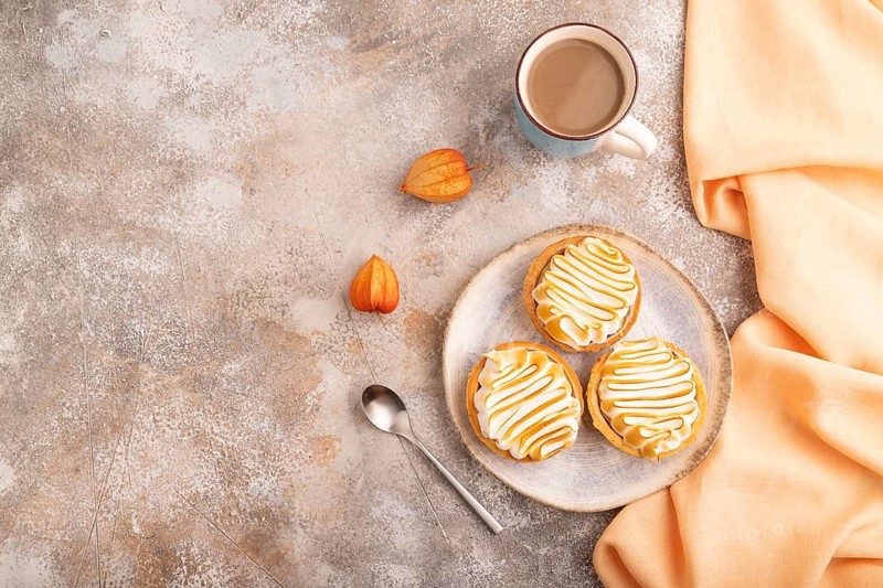 French lemon tart with meringue on brown concrete background, cup of coffee, orange linen textile, top view, flat lay, copy space