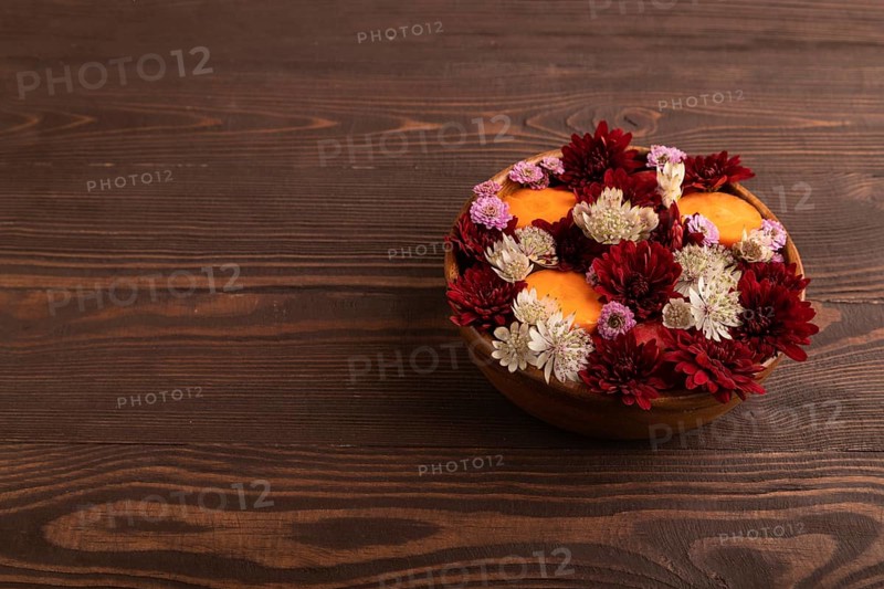 Wooden bowl with carrot slices and red Chrysanthemum flowers, Astrantia flowers, flower salad on brown wooden background, side view. copy space, minimalism