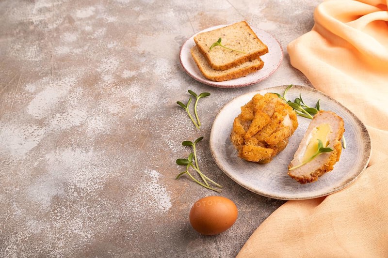 Chicken Schnitzel on blue plate with microgreen on brown concrete background and orange linen textile. side view, copy space