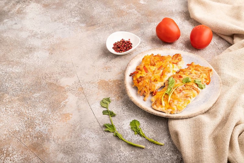 Baked chicken meat with cheese and tomatoes on brown concrete background and linen textile. side view, copy space