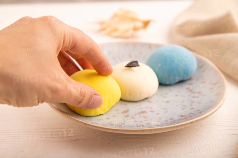 Japanese Mochi Cakes with hand on white wooden background and linen textile, side view, close up, selective focus
