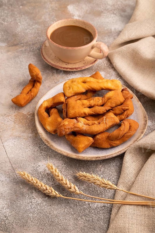 Crunchy biscuit Brushwood cookies sprinkled with powdered sugar on brown concrete background and linen textile, cup of coffee, side view, close up