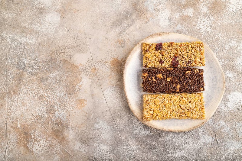 Granola bars with caramel, nuts, flakes in ceramic plate on brown concrete background. Top view, flat lay, copy space