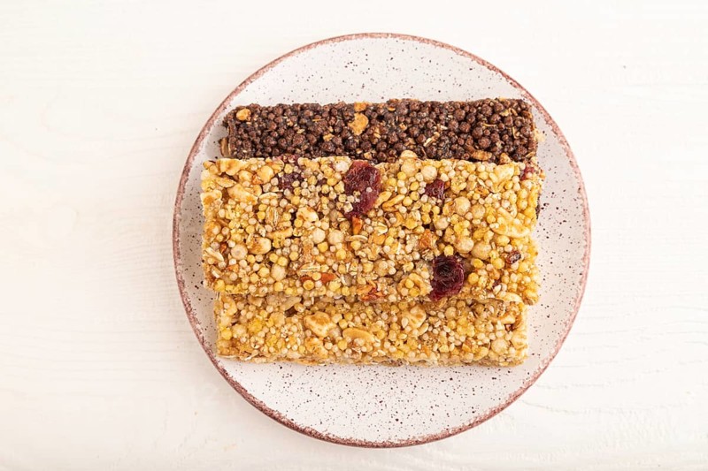 Granola bars with caramel, nuts, flakes in ceramic plate on white wooden background. Top view, flat lay, close up