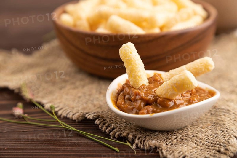 Corn flakes sticks with caramel in wooden bowl on brown wooden background and linen textile. Side view, close up, selective focus