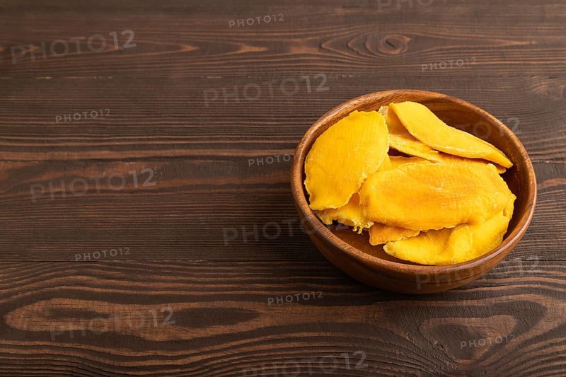 Dried Mango in wooden bowl on brown wooden background. Side view, copy space. healthy food, minimalism