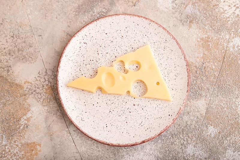 Piece of cheese with holes on ceramic plate on brown concrete background, top view, flat lay, copy space, minimalism