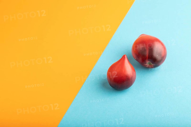Red Heart shape tomatoes on blue and orange pastel paper background. Side view, copy space. healthy food, vegetable, minimalism