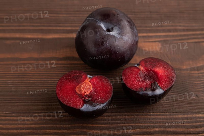 Purple Plum Cut in half on brown wooden background. Side view, close up. healthy food, vegetable, minimalism