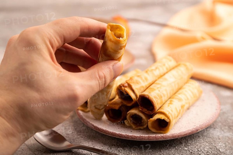 Waffles with caramel with hand on brown concrete background and orange linen textile, side view, close up, selective focus