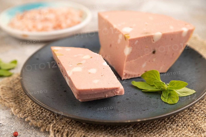 Mortadella sausage on plate with pepper and herbs on brown concrete background and linen textile. Side view, close up, selective focus