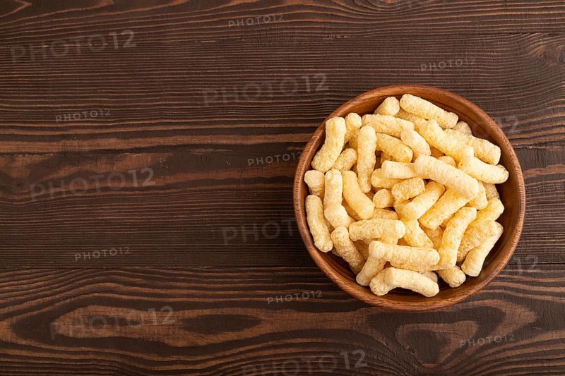 Corn flakes sticks with caramel in wooden bowl on brown wooden background. Top view, flat lay, copy space