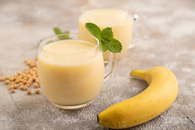 Organic non dairy banana and soy milk in glass on brown concrete background. Vegan healthy food concept, side view, close up, selective focus