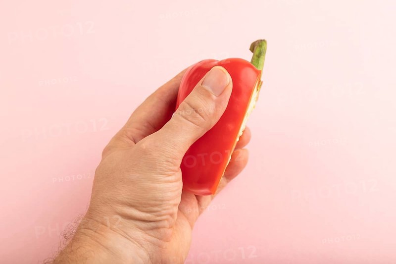 Hand holding sliced Red Cutted pepper on pink pastel background. Side view, copy space. Tropical, healthy food, vegetable, minimalism