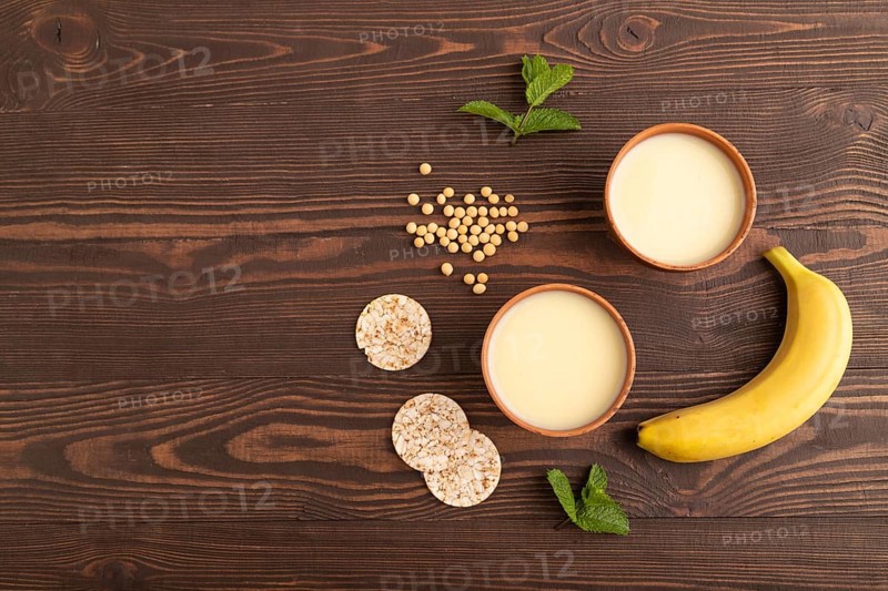 Organic non dairy banana and soy milk in clay cup on brown wooden background. Vegan healthy food concept, flat lay, top view, copy space