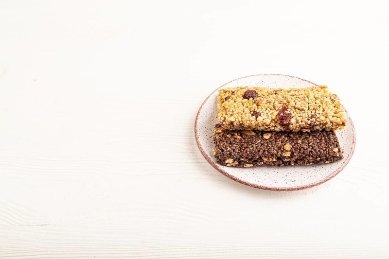 Granola bars with caramel, nuts, flakes in ceramic plate on white wooden background. Side view, copy space