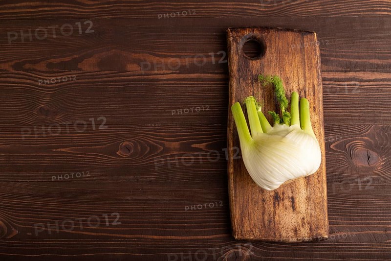 Fresh Fennel bulb on wooden cutting board on brown wooden background, top view, flat lay, copy space, minimalism