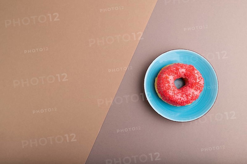 Pink Donut with sprinkles on blue ceramic plate on beige and gray pastel paper background, top view, flat lay, copy space, minimalism