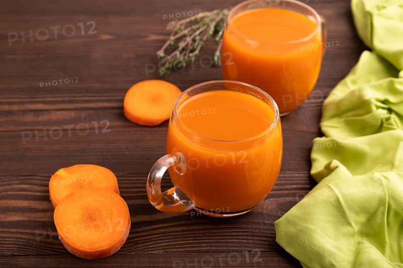 Two glasses with carrot juice, on wooden background and green textile. Diet, healthy eating concept. side view, close up, minimalism