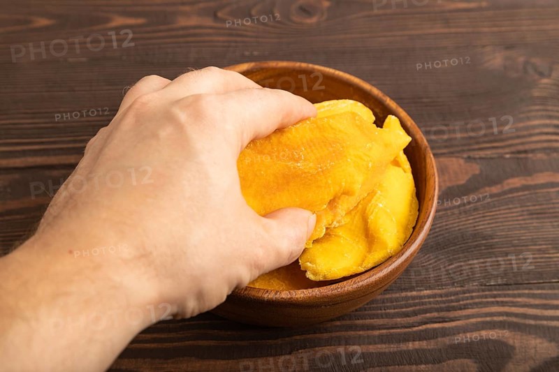 Dried Mango in wooden bowl with hand on brown wooden background. Side view, close up. healthy food, minimalism
