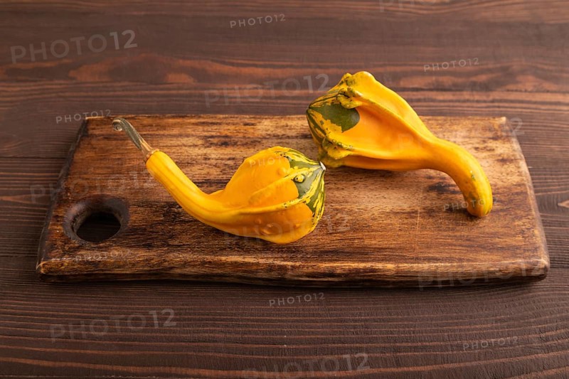 Two decorative orange Pumpkins on cutting board on brown wooden background, side view, close up, minimalism