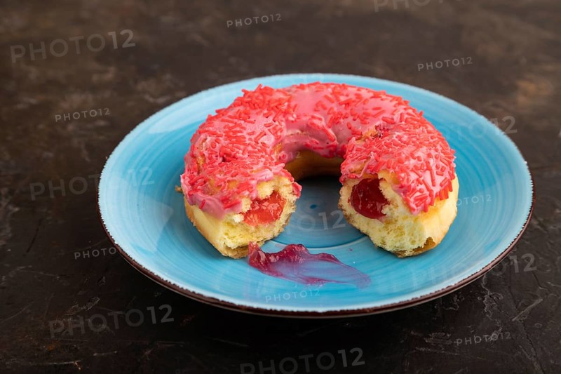 Bitten Pink Donut with sprinkles on blue ceramic plate on black concrete background, side view, close up, minimalism
