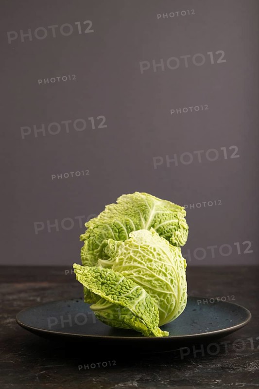 Green lettuce on blue plate on black concrete background. Side view, copy space. healthy food, vegetable, minimalism, low key