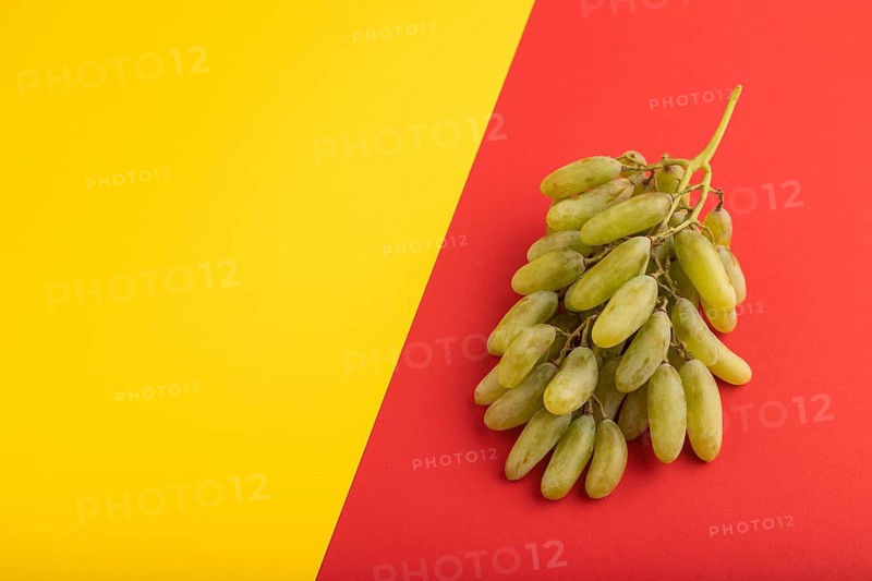 Green grapes on yellow and red paper pastel background. Side view, copy space. healthy food, minimalism