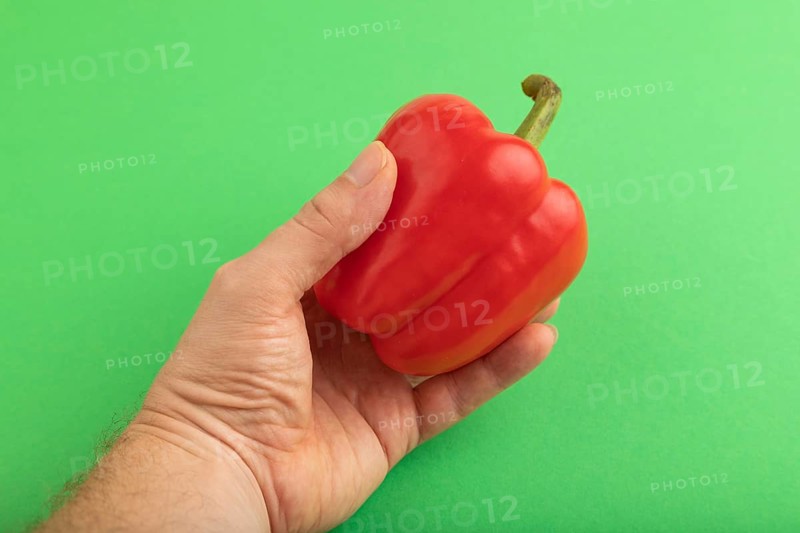 Hand holding Red pepper on green pastel background. Side view, copy space. healthy food, vegetable, minimalism