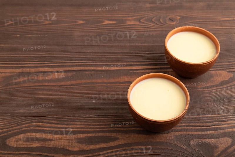Organic non dairy banana and soy milk in clay cup on brown wooden background. Vegan healthy food concept, flat lay, side view, copy space