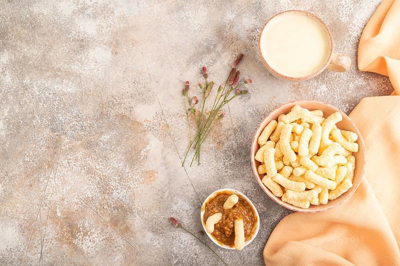 Corn flakes sticks with caramel in ceramic bowl on gray concrete background and orange linen textile. Top view, flat lay, copy space