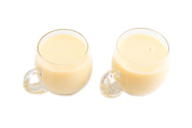 Organic non dairy banana and soy milk in glass cup on brown wooden background. Vegan healthy food concept, flat lay, side view, copy space