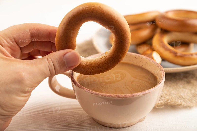 Homemade Ring Bagel with hand with cup of coffee on white wooden background and linen textile. side view, close up, selective focus