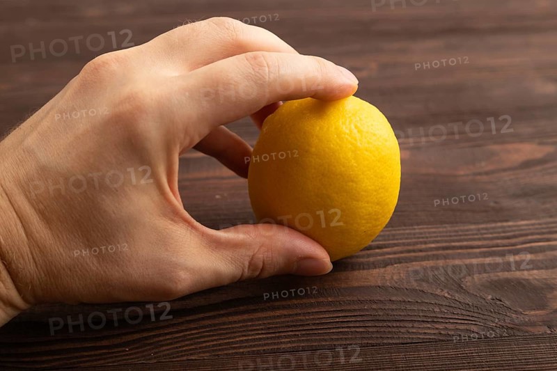 Yellow Lemon Cut in half with hand on brown wooden background. Side view, close up. healthy food, vegetable, minimalism. citrus