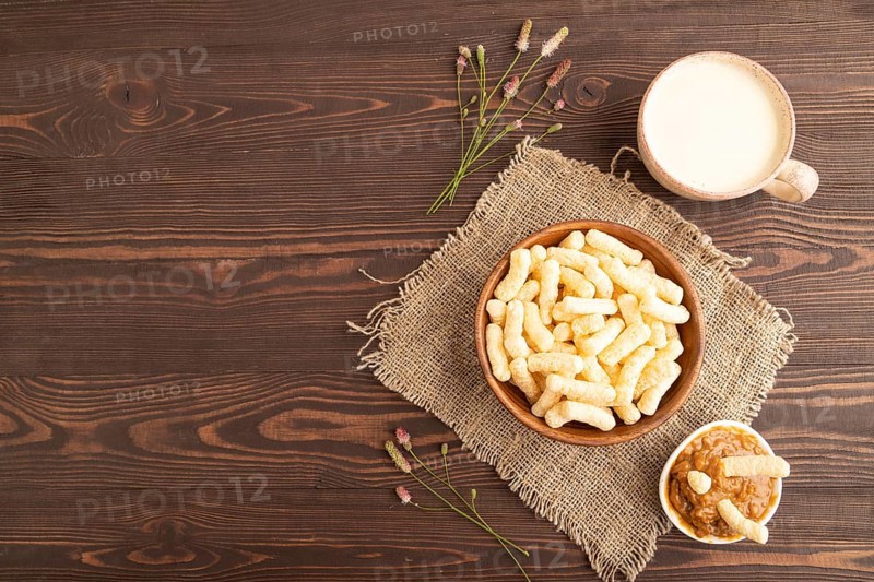 Corn flakes sticks with caramel in wooden bowl on brown wooden background and linen textile. Top view, flat lay, copy space
