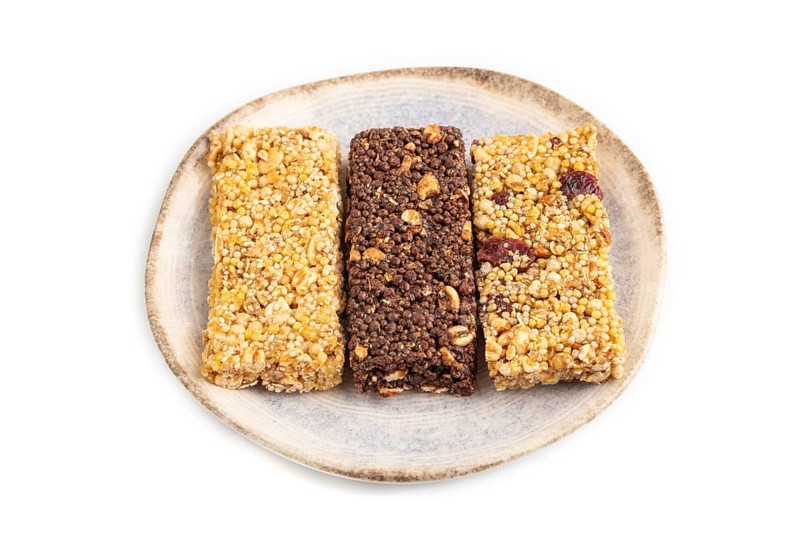 Granola bars with caramel, nuts, flakes in ceramic plate isolated on white background. Side view, close up