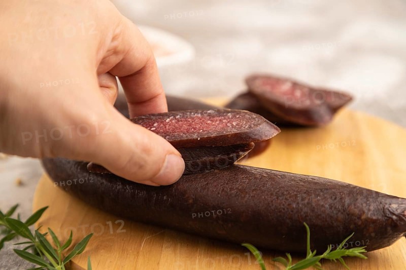 Sujuk sausage with hand on wooden cutting board with pepper and herbs on brown concrete background. Side view, close up, selective focus