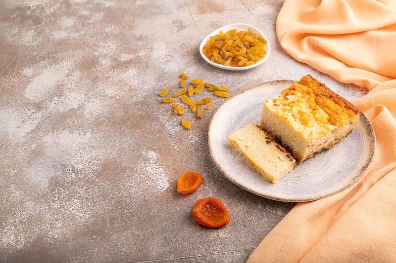 ?ottage cheese ?asserole, Curd cake, with dried apricots and raisins on brown concrete background and orange textile, side view, copy space, minimalism