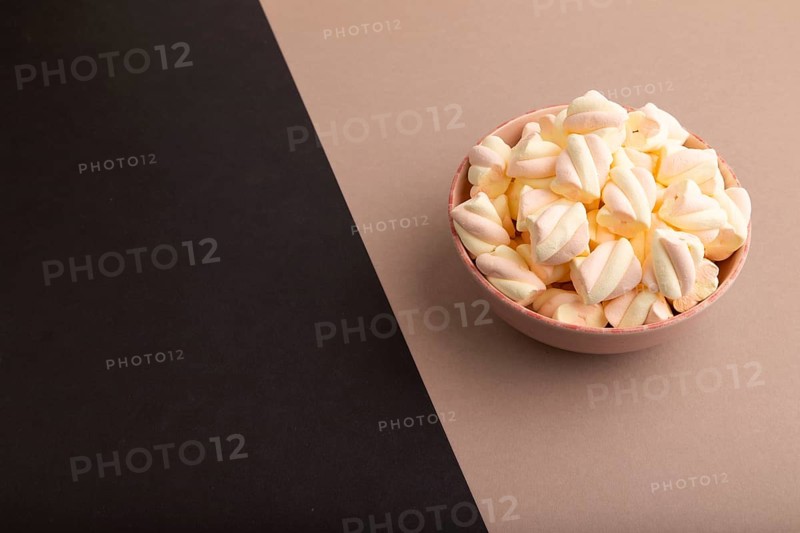 Orange and pink marshmallow in ceramic bowl on black and beige pastel paper background, side view, copy space, minimalism