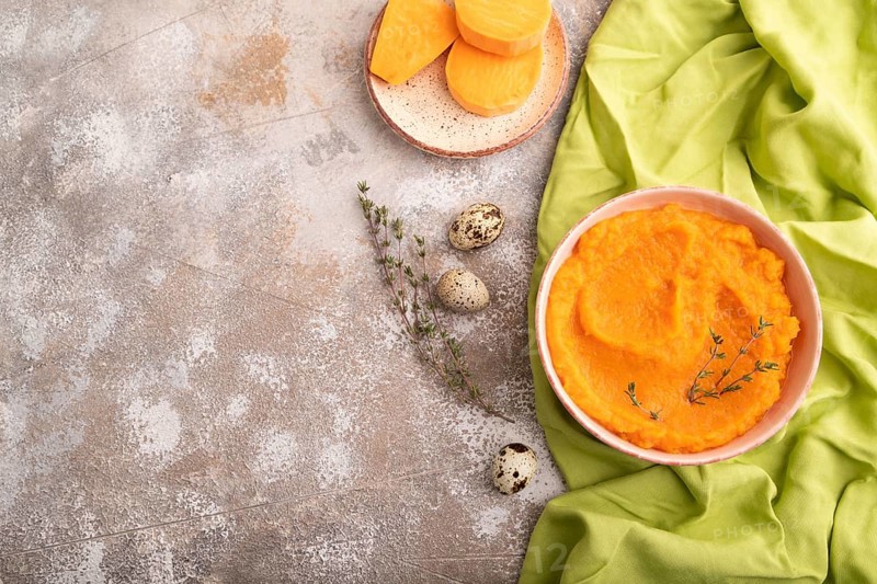 Sweet potato porridge in ceramic bowl on brown concrete background and green textile. Diet, healthy eating concept. top view, flat lay, copy space