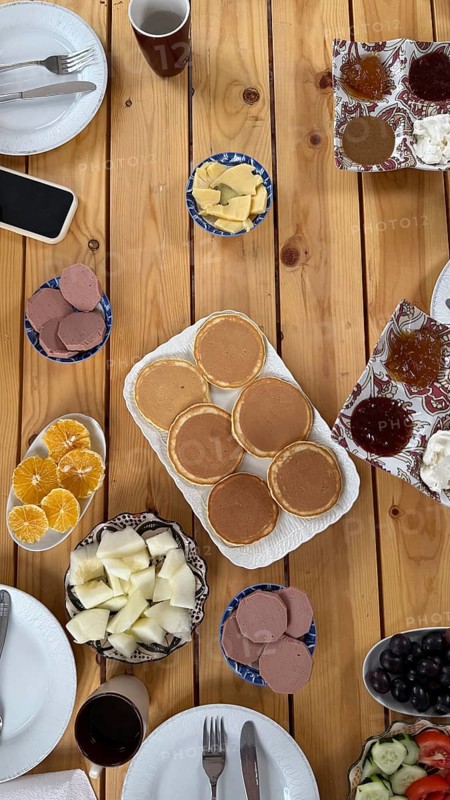 Wooden table spread of traditional moroccan breakfast, pancakes, sliced oranges and melon, olives, cucumber and tomato salad, cheeses, jams and butter in a colorful morning feast