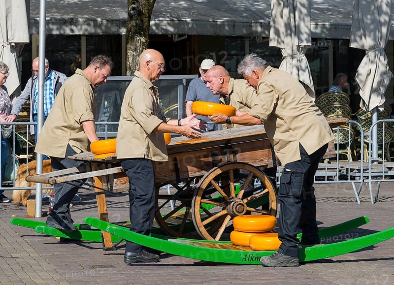 Männer in beiger Kleidung stapeln Käseräder auf einem traditionellen Holzwagen, Käse, Käsemarkt, Alkmaar, Alkmar, Noord-Holland, Nordholland, Niederlande