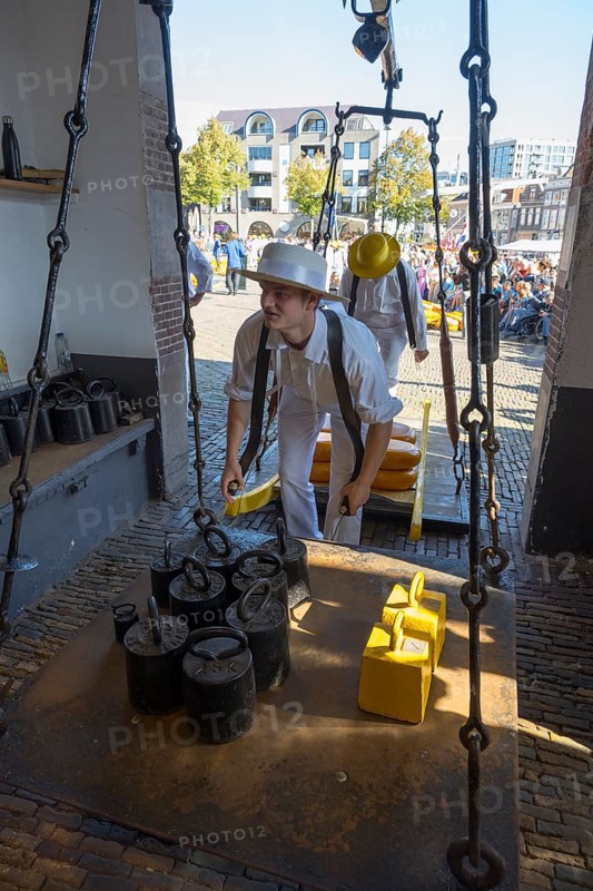 Ein Mann in historischer Kleidung wiegt Käse auf einem alten Markt mit anderen Teilnehmern, ehemalige Stadtwaage, Käse wiegen, Käseträger, Käse, Käsemarkt, Alkmaar, Alkmar, Noord-Holland, Nordholland, Niederlande