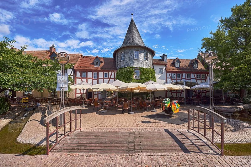 Fachwerkhäuser, Turm, Häuserzeile, Fußgängerbrücke, Holzbrücke, hölzern, Altstadt, historische Gebäude, Gehweg aus Klinker, Pflastersteine, Restaurant Zum Türmchen, Außenbereich einer Gastronomie mit Sonnenschirmen, Tischen und Stühlen, blauer Himmel, Cumuluswolken, Cirrostratuswolken, Platz am Untertor, Burggrabenstraße, Hofheim am Taunus, Main-Taunus-Kreis, Hessen, Deutschland