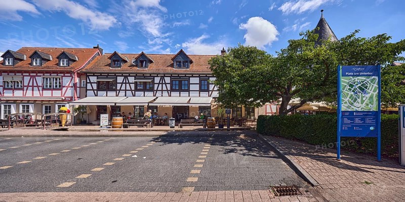Platz am Untertor, Fachwerkhäuser, Häuserzeile, historische Gebäude, Gauben, Eisdiele, Außenbereich einer Gastronomie, Parkplatz, Standorttafel, Bäume, Hecke, blauer Himmel, Cumuluswolken, Burggrabenstraße, Hofheim am Taunus, Main-Taunus-Kreis, Hessen, Deutschland