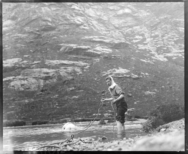 Person crawling across river stream secured by man holding a rope mountain exploration c 1900 possibly Cuillin mountains, Skye, Scotland, UK