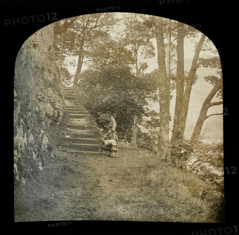 Magic lantern slide of woman standing in countryside next to a flight of steps through woodland, possibly the Lake District, England, UK c 1900