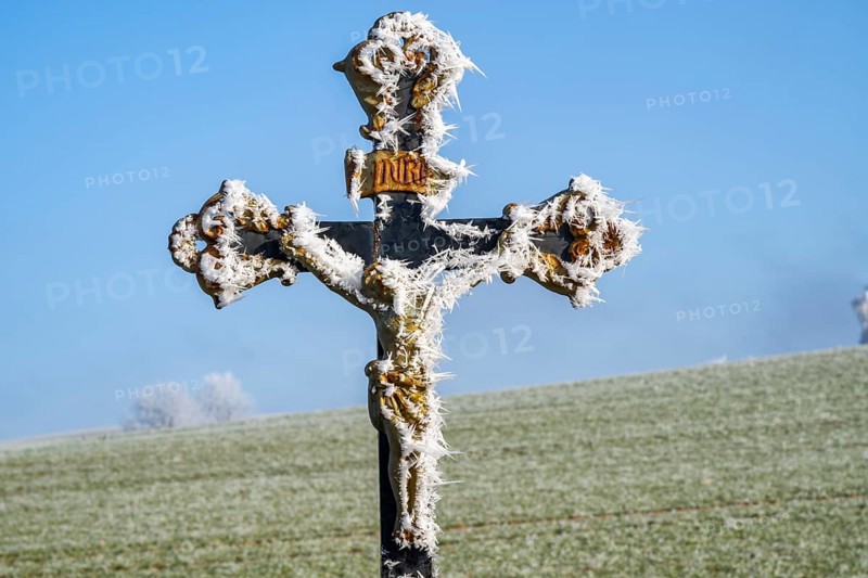 Crucifix with hoarfrost in front of blue sky at sunshine in winter, Bavaria, Germany