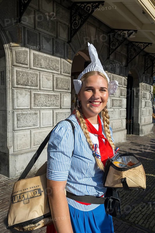 Woman in traditional dress and headdress smiling in front of a historic building, former city weigh house, cheese market, Alkmaar, Alkmar, Noord-Holland, North Holland, Netherlands