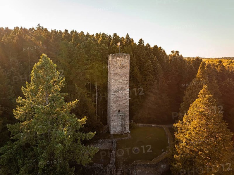An old tower rises out of the dense forest, illuminated by the warm rays of the evening sun, Mandelberg castle ruins, Pfalzgrafenweiler, Germany